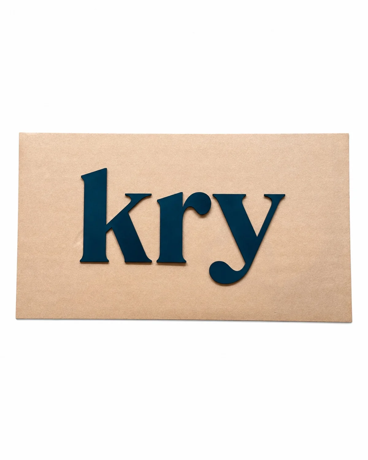 Lettrage « kry » en plexiglas peint bleu foncé, disposé sur un gabarit de placement en carton.